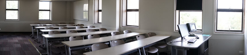 Medium room with rows of long tables with chairs and a presenters desk upfront